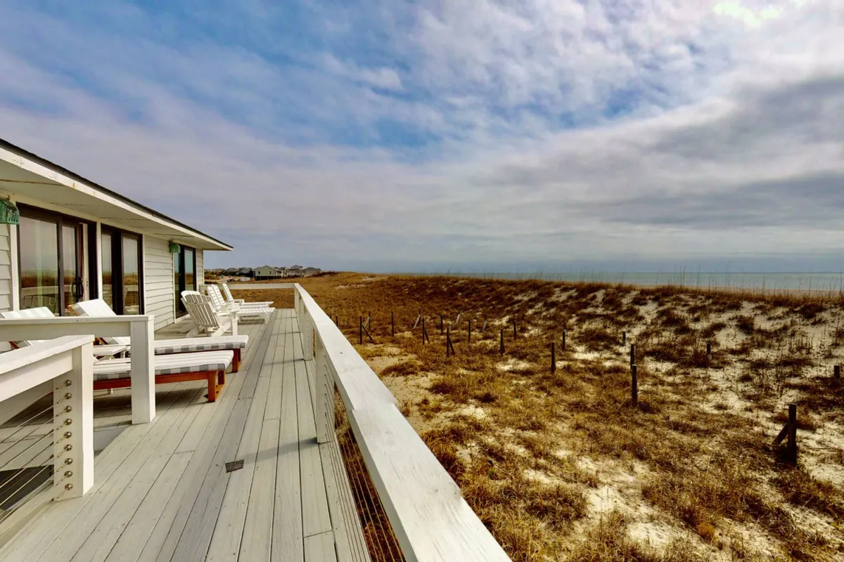 A set of comfortable deck chairs positioned on a balcony with views of the dunes and the wide ocean horizon beyond, suggesting a peaceful spot for sunbathing, reading, or simply enjoying the breeze and sunsets.