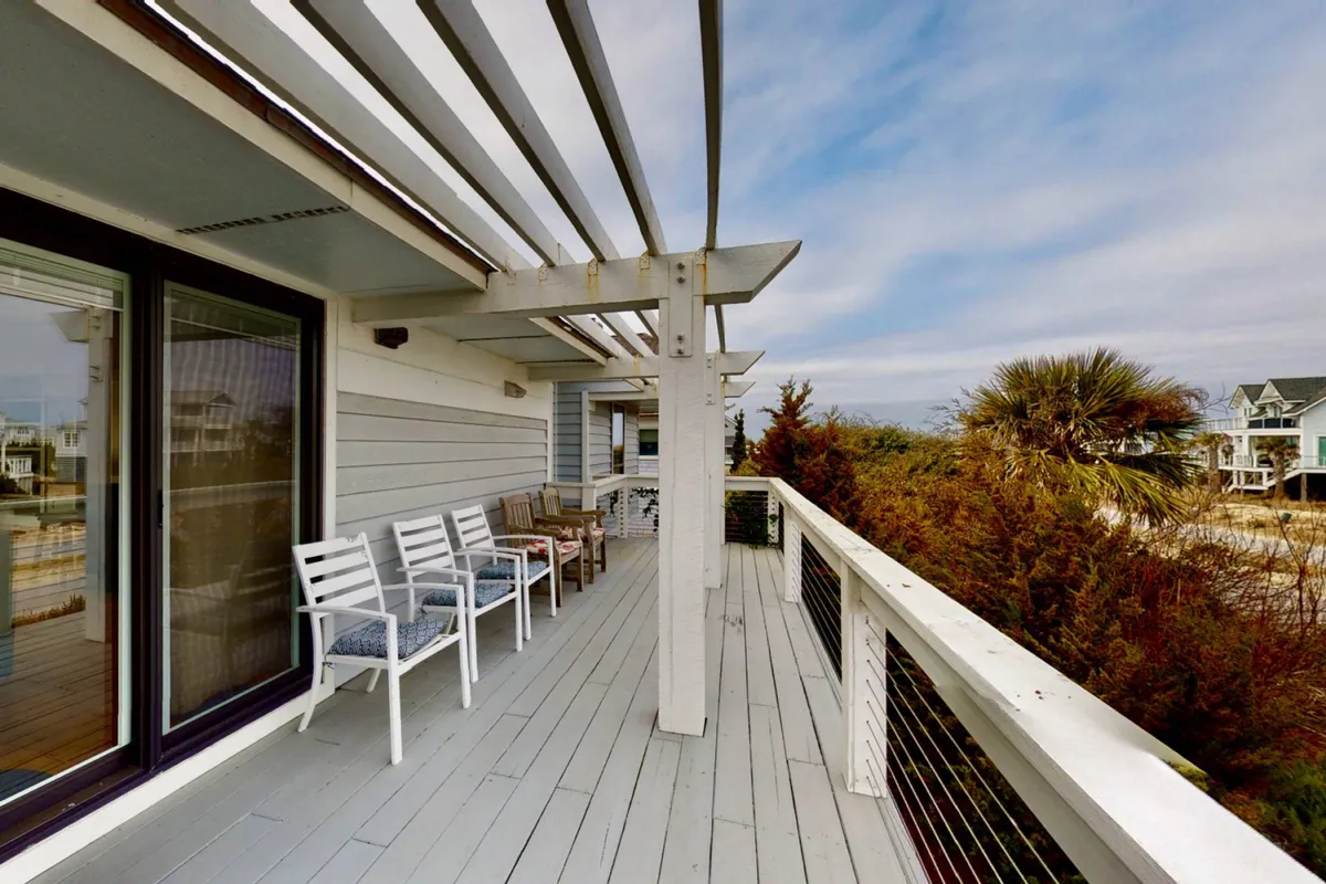 A spacious deck overlooking the ocean is framed by lush greenery. Comfortable seating invites relaxation and gathering, while the vast sea beyond hints at panoramic views stretching to the horizon—perfect for grandparents watching over family activities below.