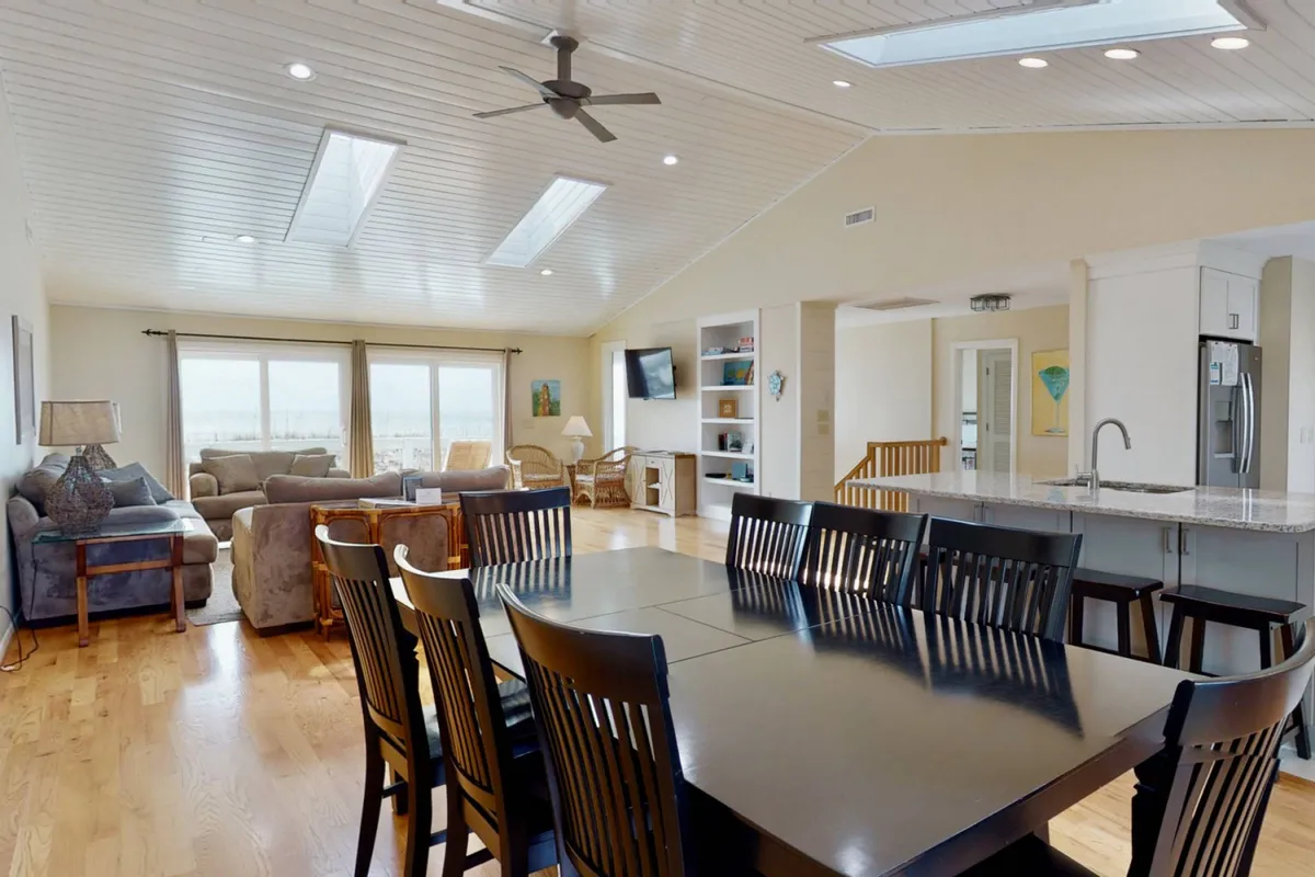 A broad dining area seamlessly adjoining a cozy living room and a modern kitchen with an island. Large windows welcome in natural light and frame the shared spaces, ideal for meals and socializing.