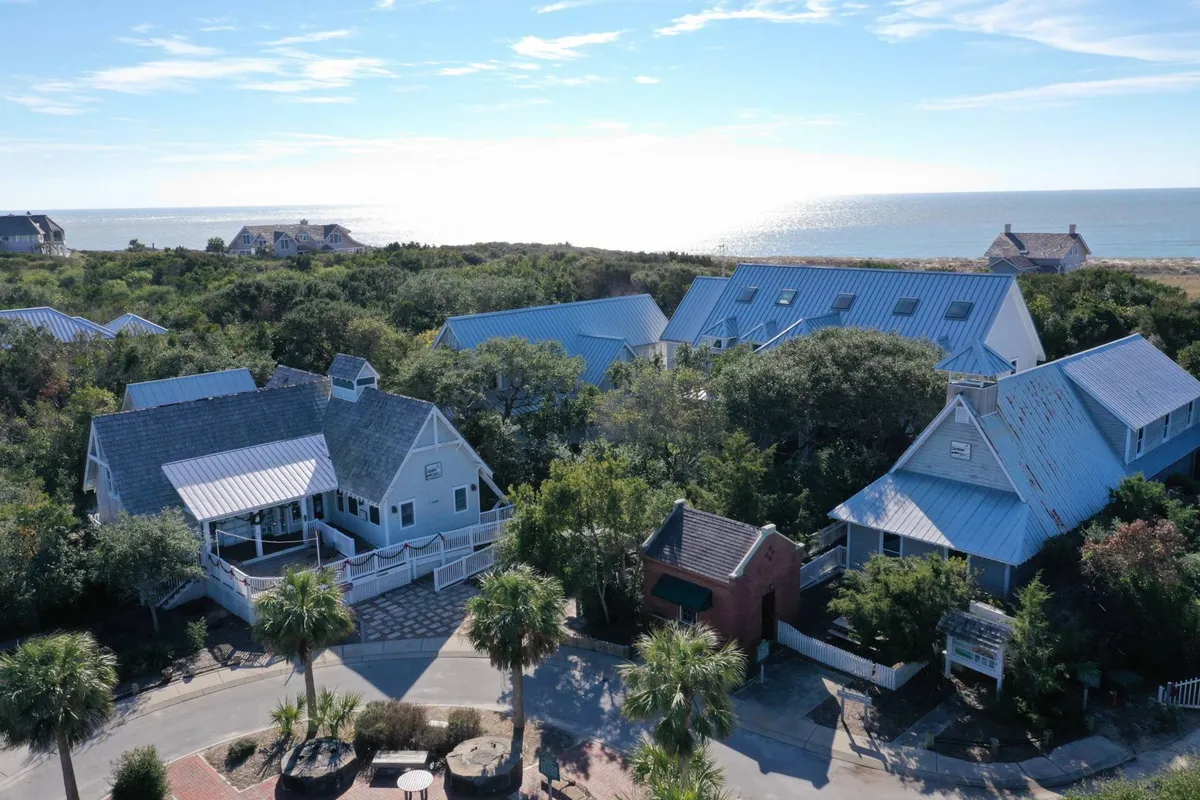 This exterior image features a sweeping ocean view framed by lush greenery, a paved pathway, and a collection of coastal homes with varying architectural styles. The tranquil setting hints at relaxed outdoor activities like dining al fresco, morning walks, or quiet conversations while enjoying nature.