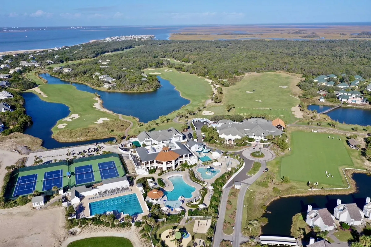This vibrant exterior shot showcases lush green golf courses, sparkling swimming pools, tennis courts, water features, and surrounding natural landscapes. The scene suggests a range of outdoor and resort-style activities available nearby.