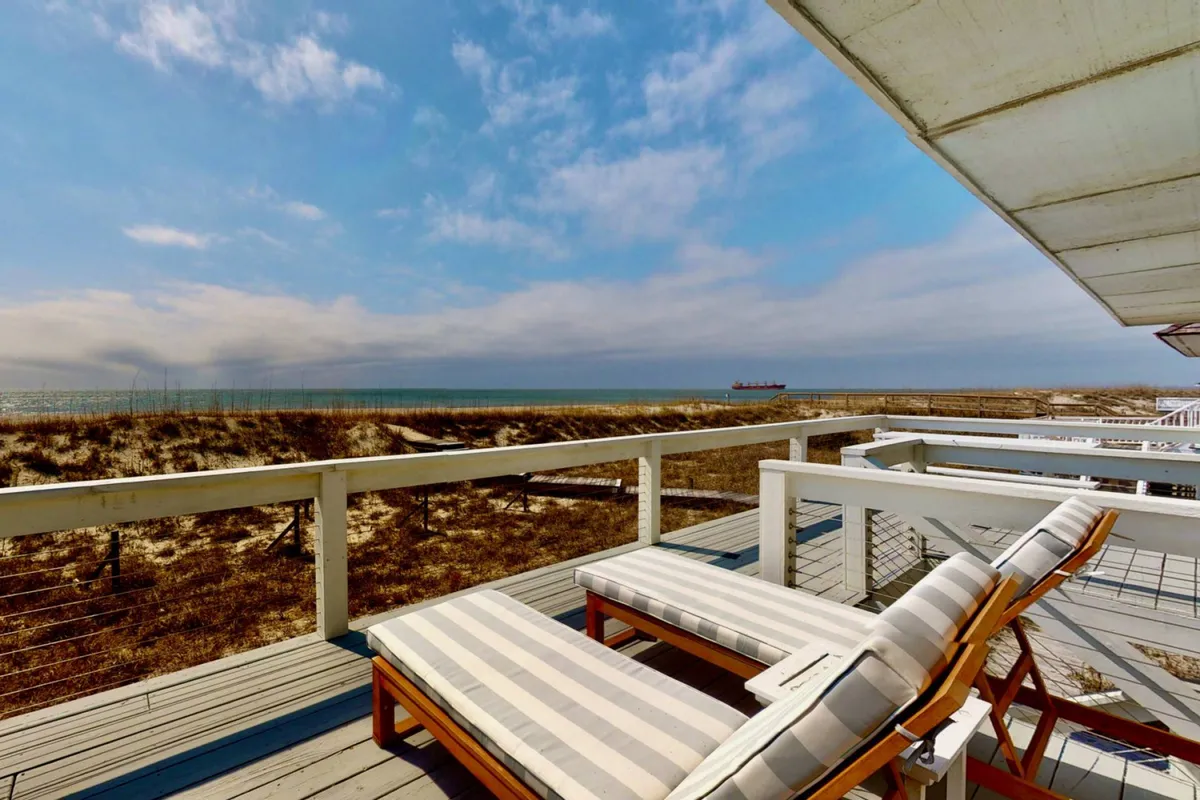 A serene exterior shot showing deck chairs facing the ocean, surrounded by dune grass and open sky. The view invites visitors to unwind outdoors, breathe in the ocean air, and enjoy the natural setting.